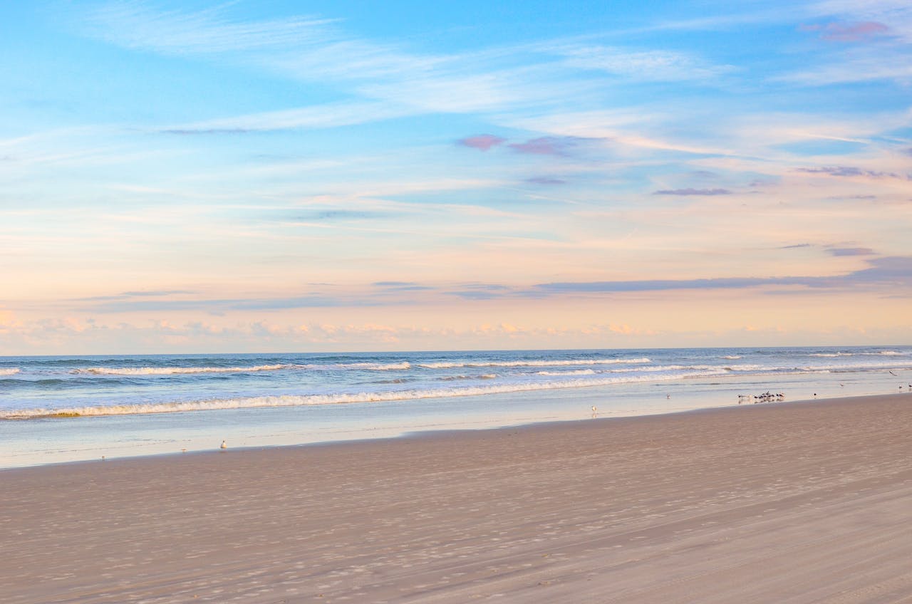Peaceful beach scene with soft waves and pastel skies at sunrise, ideal for relaxation themes.