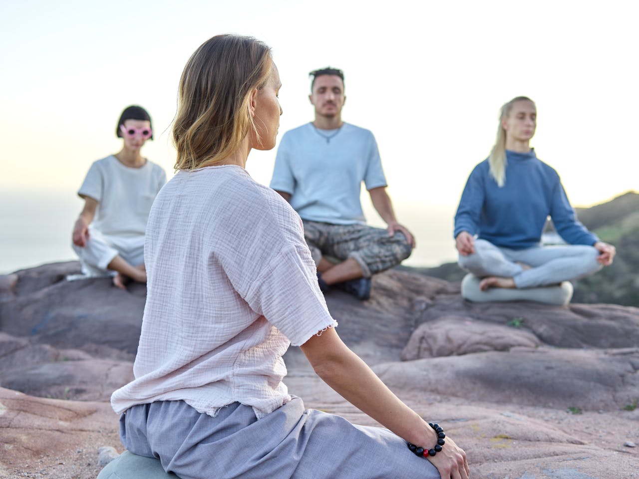 About Group of adults meditating on a rocky cliff at sunset, embracing relaxation and spirituality.